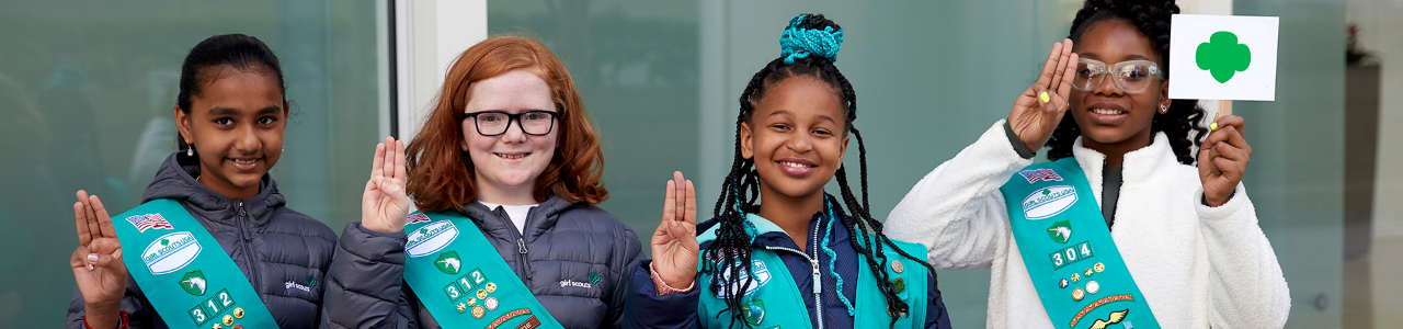  junior girl scouts displaying the girl scout sign with hands 