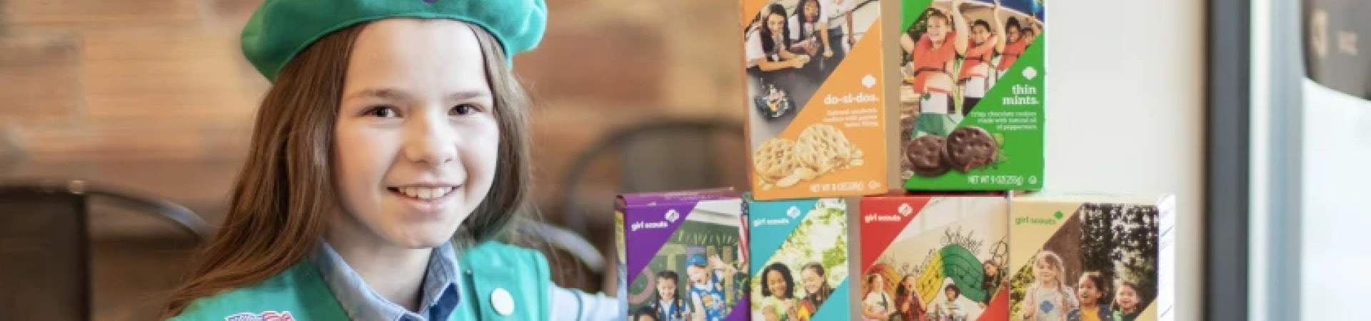  girl scout ellisyn sitting at a table with boxes of girl scout cookies 