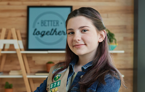 girl scout wearing a sash standing in front of a bookshelf