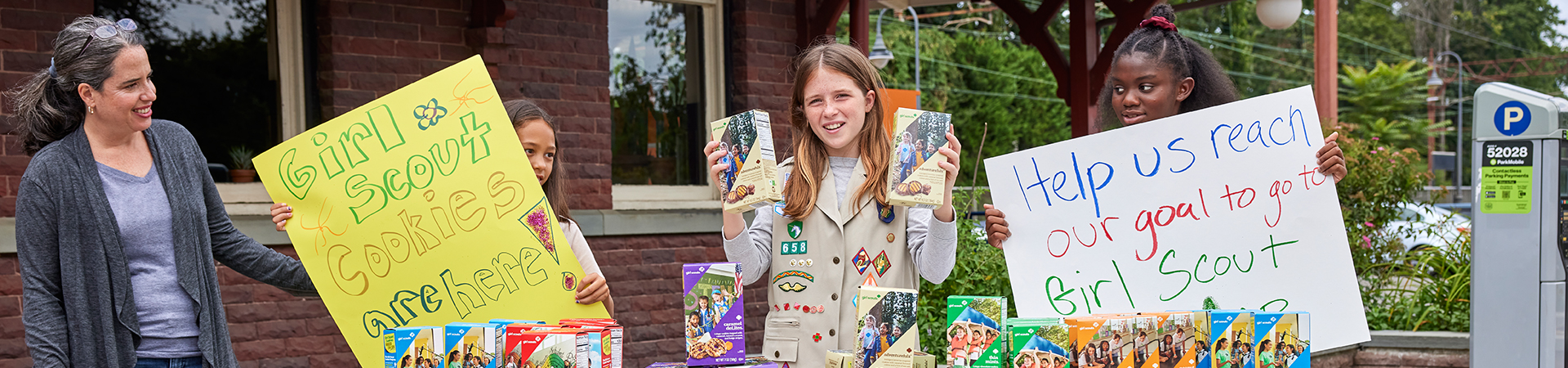  girl scouts at a cookie booth holding signs and cookies 