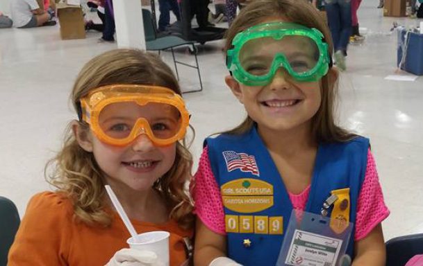 Girl Scouts sit on cement steps smiling and hugging.