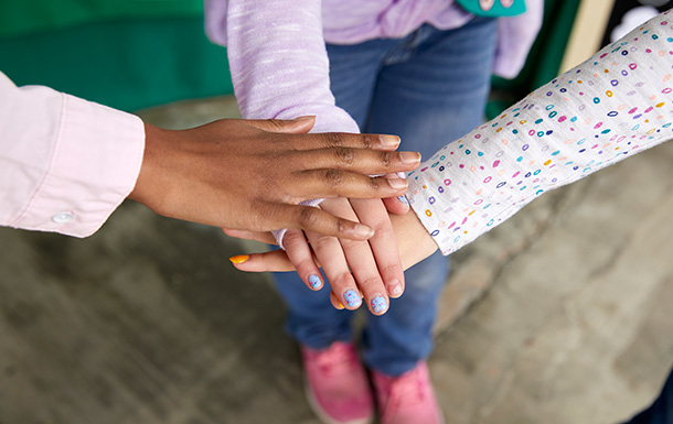 girls in a circle with one hand stacked on each other